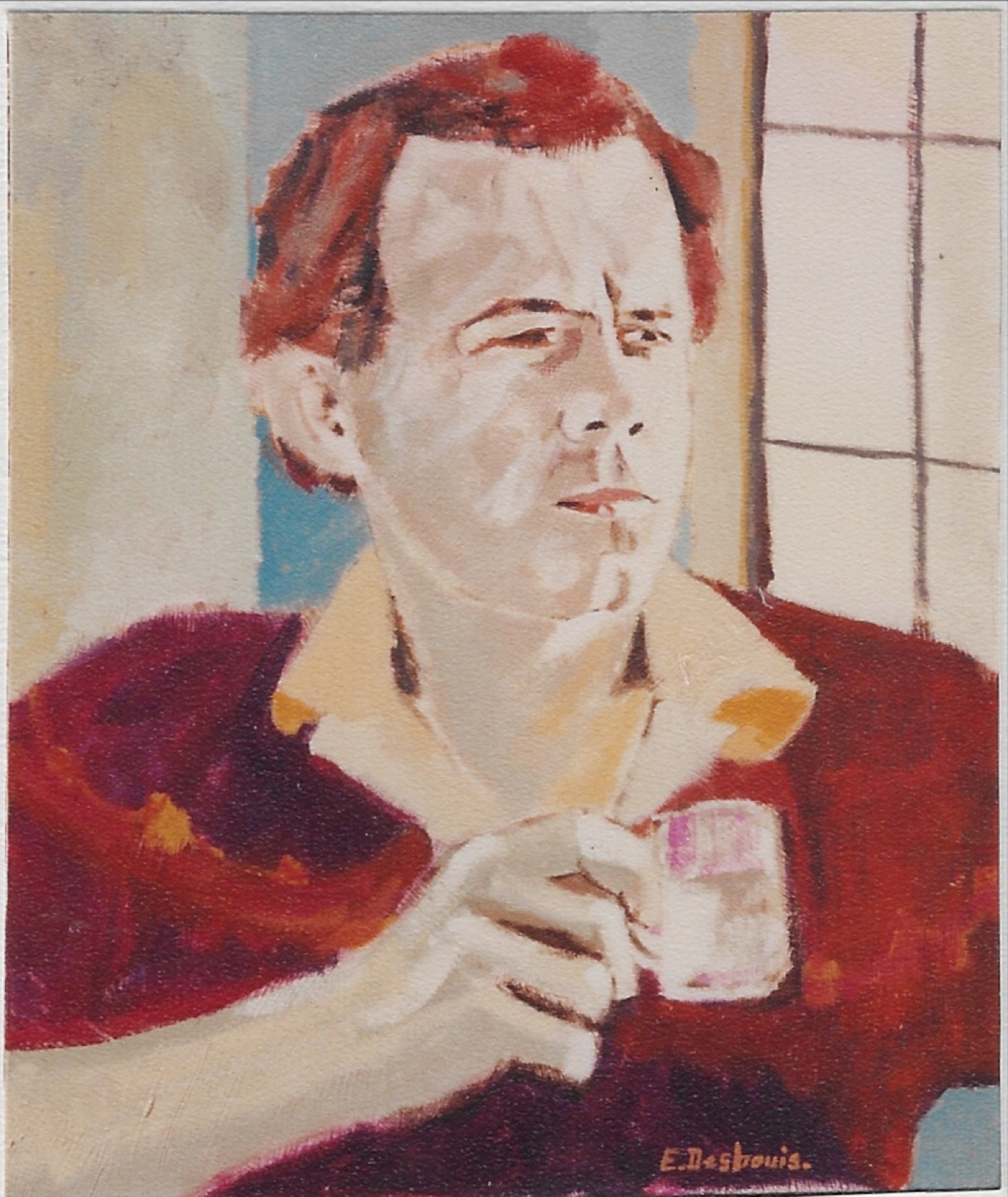 Buste de l’artiste col de chemise crème sur pull bordeaux, une tasse blanche dans la mais droite, regard lointain, fenêtre sur la droite.